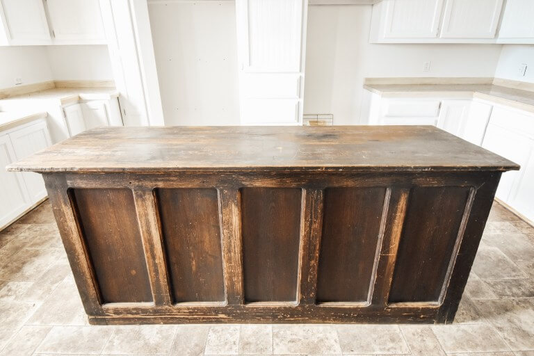 A rustic wooden kitchen island in an empty kitchen with white cabinets and beige countertops.