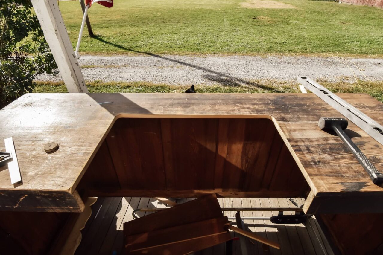 A wooden surface with a rectangular cutout, tools scattered on top, and a grassy yard with an American flag in the background.