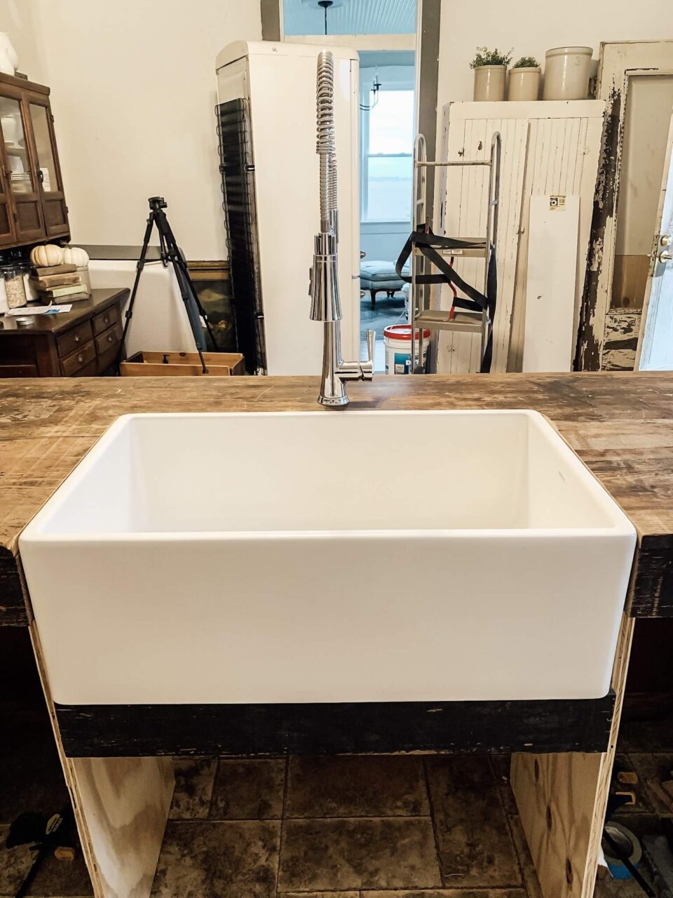 A newly installed white farmhouse sink with a tall chrome faucet in a rustic kitchen setting.