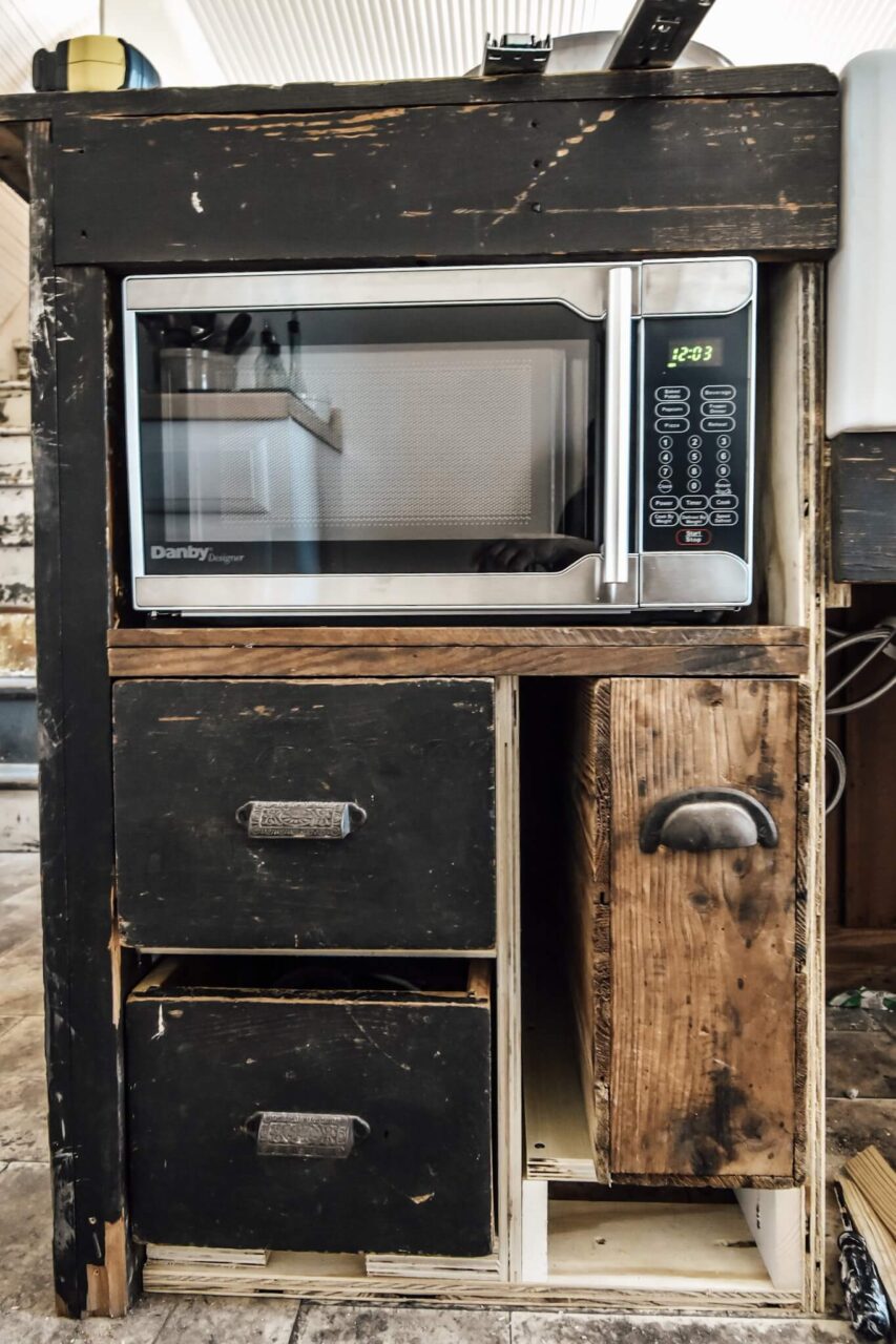A microwave installed in a rustic wooden cabinet with drawers and compartments in various stages of construction.