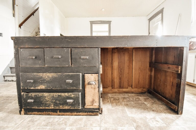 A rustic wooden kitchen island with drawers and cabinets in an empty room with tiled flooring.
