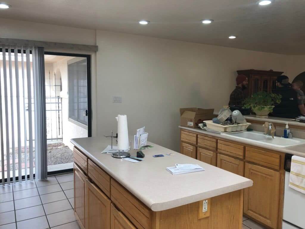 A kitchen with wooden cabinets, a countertop, a dish drying rack, and sliding glass doors to the outside.