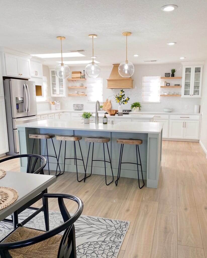 A spacious kitchen with a large island featuring bar stools, pendant lights, white cabinets, wooden accents, and stainless steel appliances.