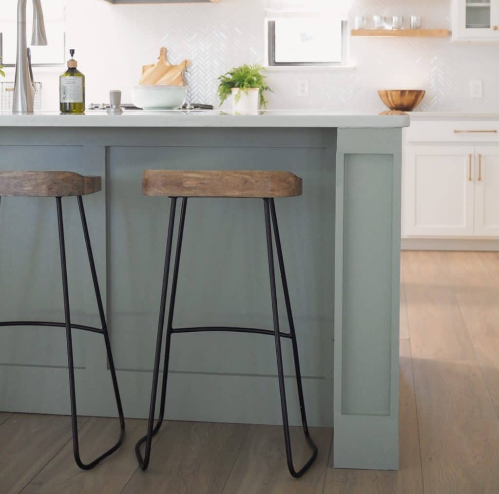 Two wooden bar stools with black metal legs at a kitchen island, with a view of the countertop and kitchen items in the background.
