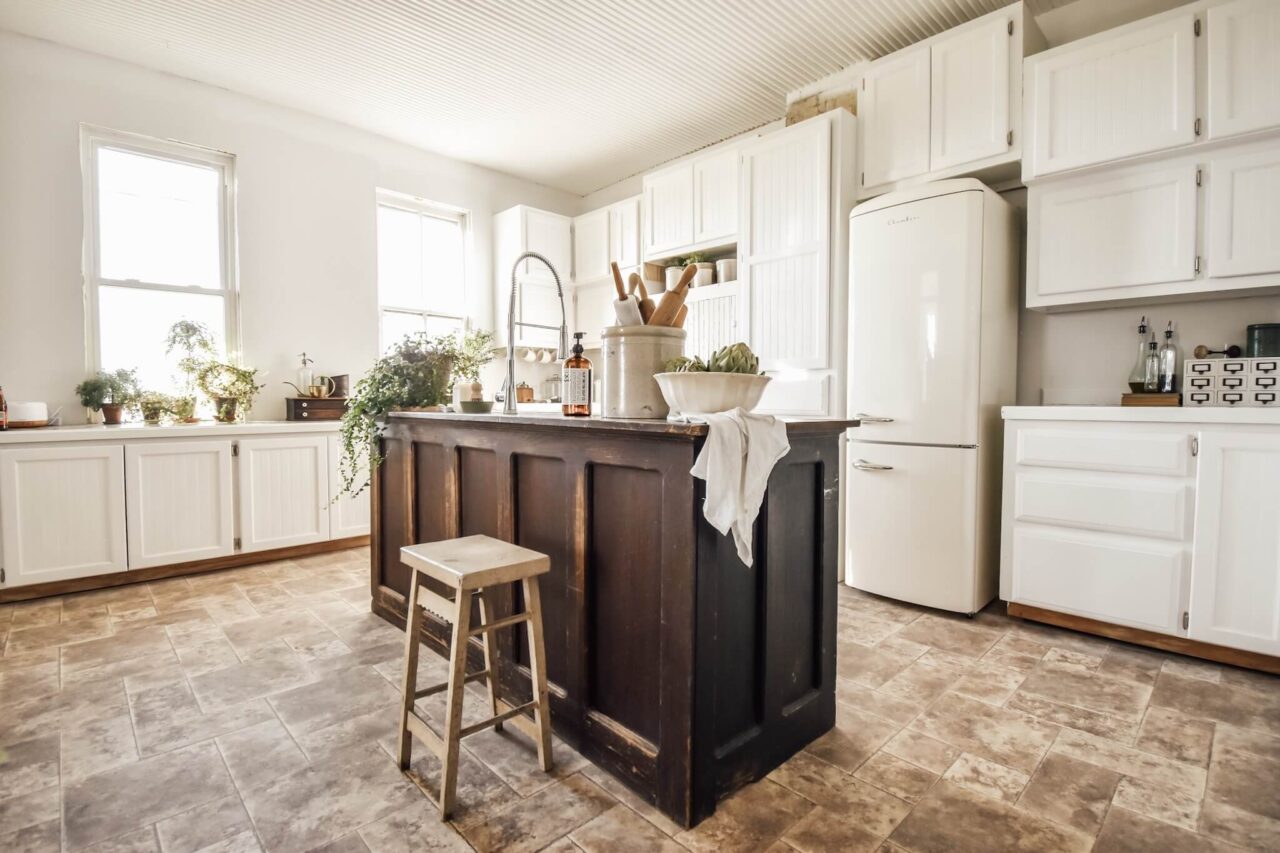 A bright kitchen with white cabinets, a rustic wooden island, a farmhouse sink, and various plants on the countertops.
