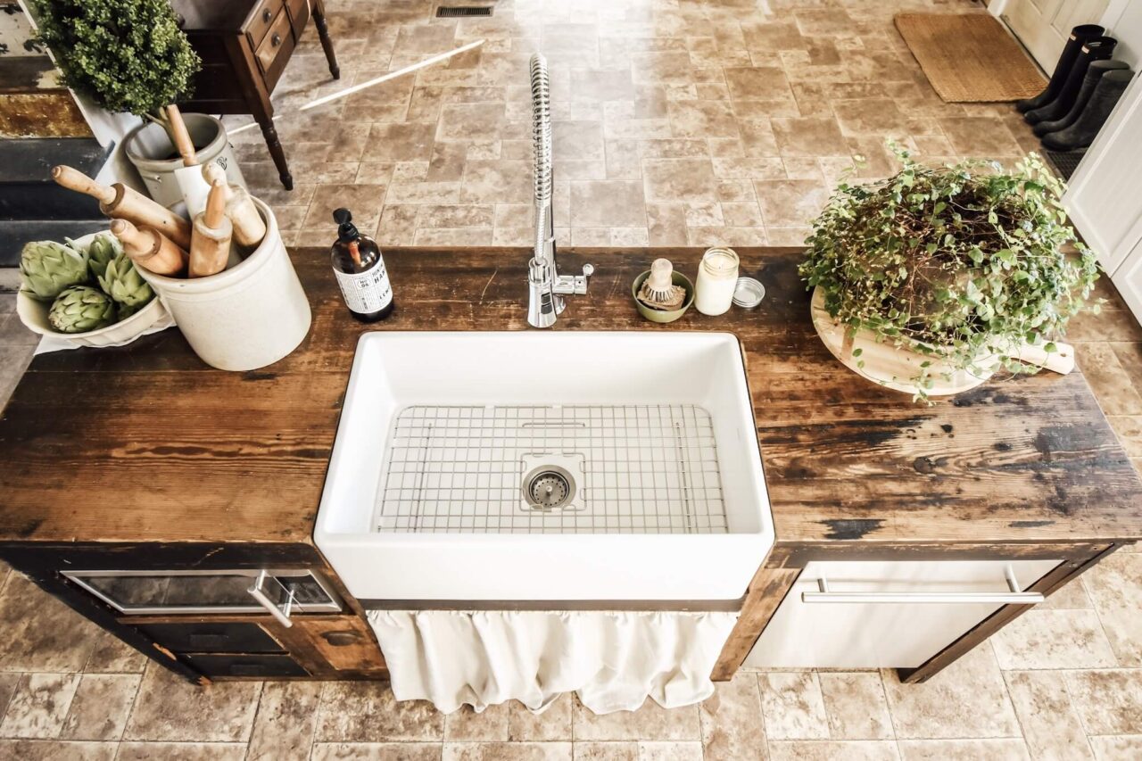 A top-down view of a rustic kitchen island with a white farmhouse sink, decorated with rolling pins, artichokes, a plant, and a bottle of dish soap.