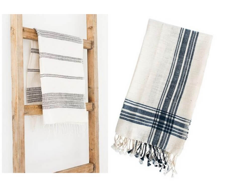 Two striped kitchen towels: one hanging on a wooden ladder and the other folded, both featuring simple black and white patterns with fringed edges.