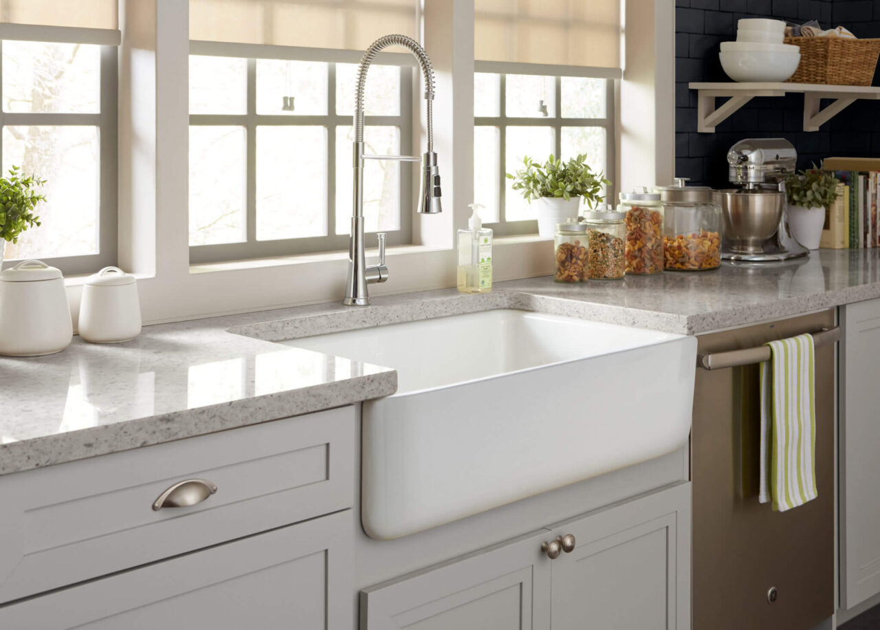 A bright kitchen with a large farmhouse sink, modern faucet, and various items on the countertop.