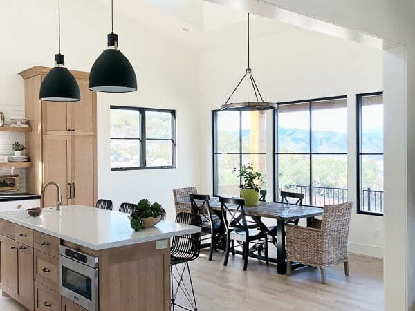A modern kitchen with a large island and pendant lights, adjacent to a dining area with a wooden table and wicker chairs.