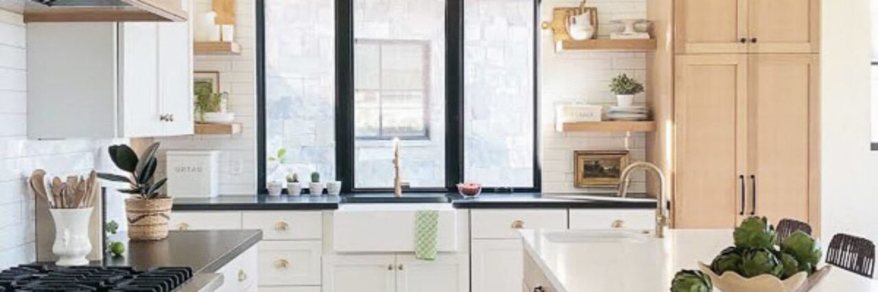 A modern kitchen with white cabinets, a farmhouse sink, and decorative plants.