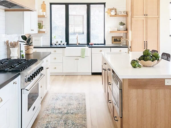 A modern kitchen with white cabinets, a black countertop, a large island, and a farmhouse sink under a large window.