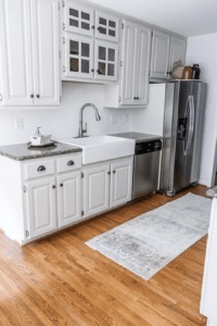 a white fireclay kitchen sink with a stainless steel faucet in a white painted kitchen