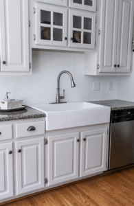 a white fireclay kitchen sink with a stainless steel faucet in a white painted kitchen