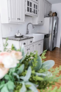a white fireclay kitchen sink with a stainless steel faucet in a white painted kitchen
