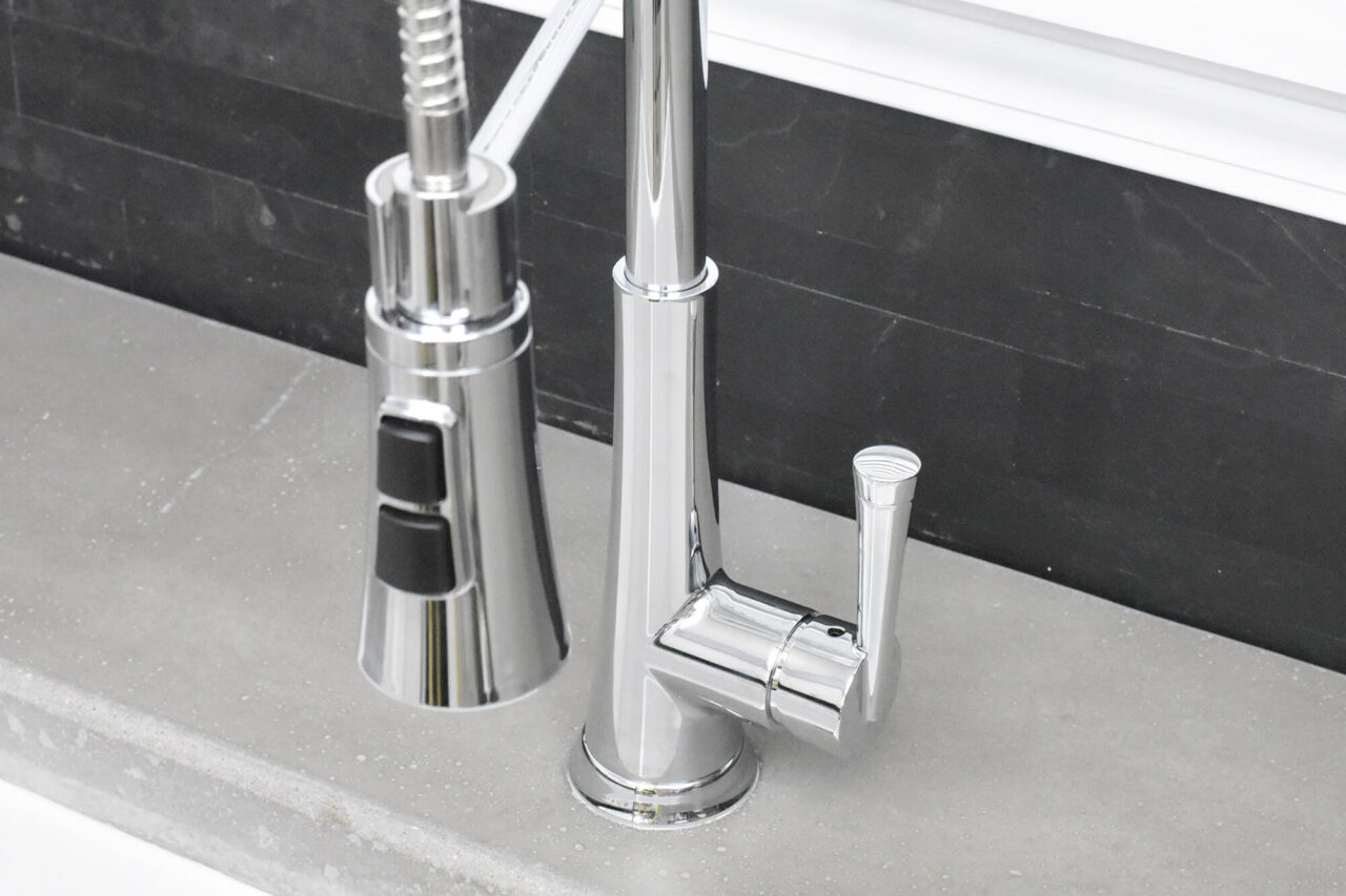 A close-up of a modern chrome spring faucet on a concrete countertop, set against a dark backsplash.