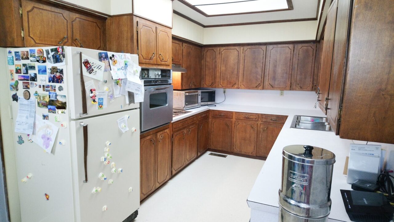 A traditional kitchen with wooden cabinets, white countertops, a white refrigerator covered with magnets and notes, and various appliances including an oven and microwave.