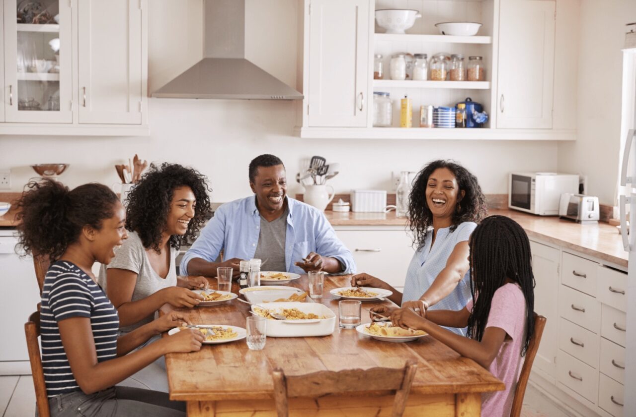a family sitting at a dining table in the kitchen enjoying a meal together