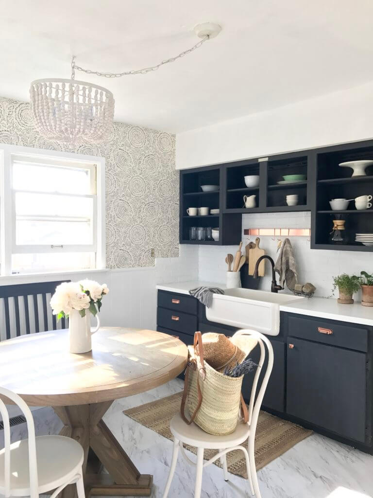 Bright kitchen with a round wooden dining table, black open cabinets, white countertops, and a farmhouse sink.