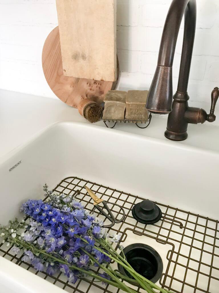 Bronze faucet over a farmhouse sink with purple flowers and soap bars on the counter.
