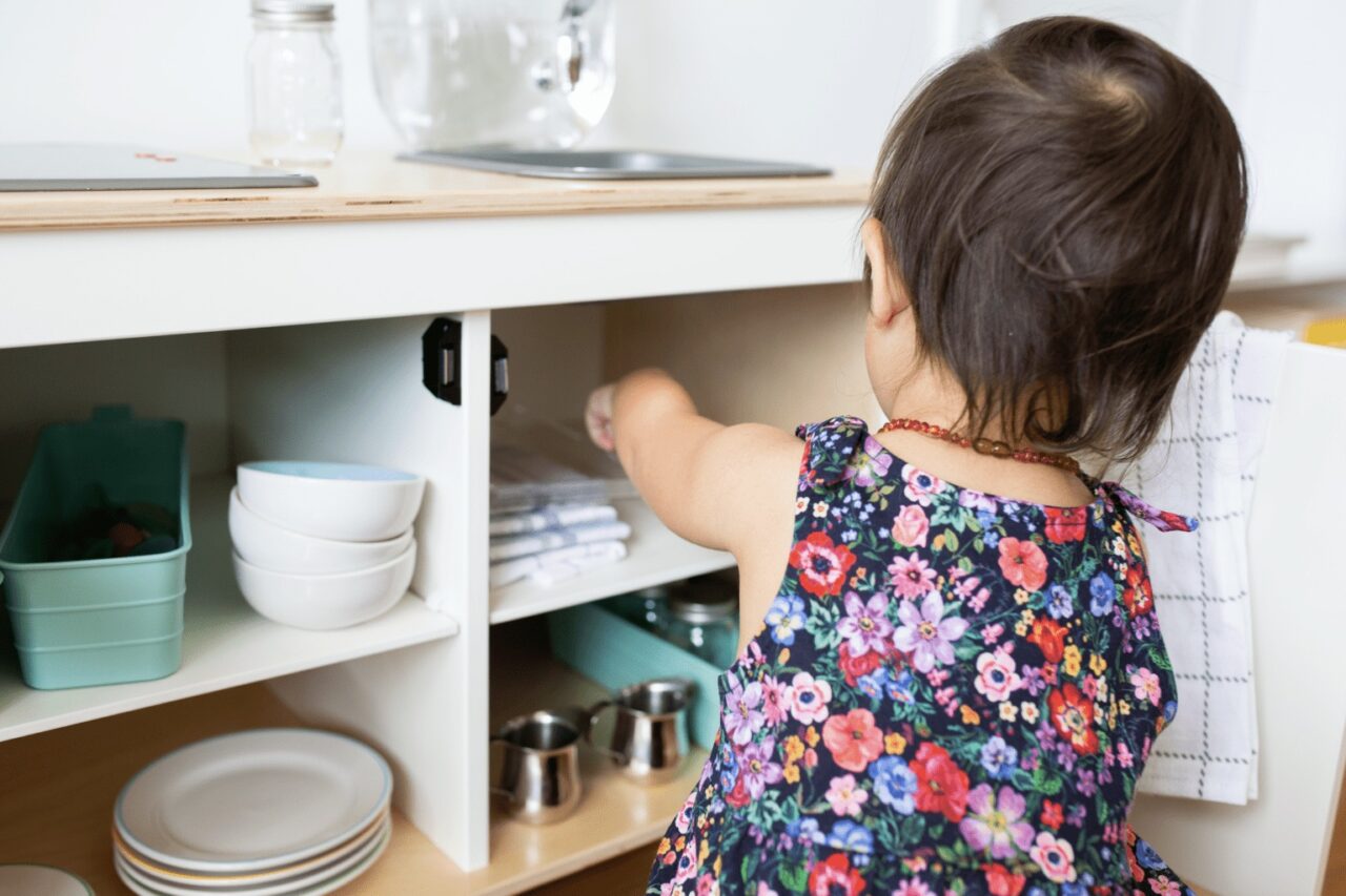 a toddler putting away dishes in a cabinet.