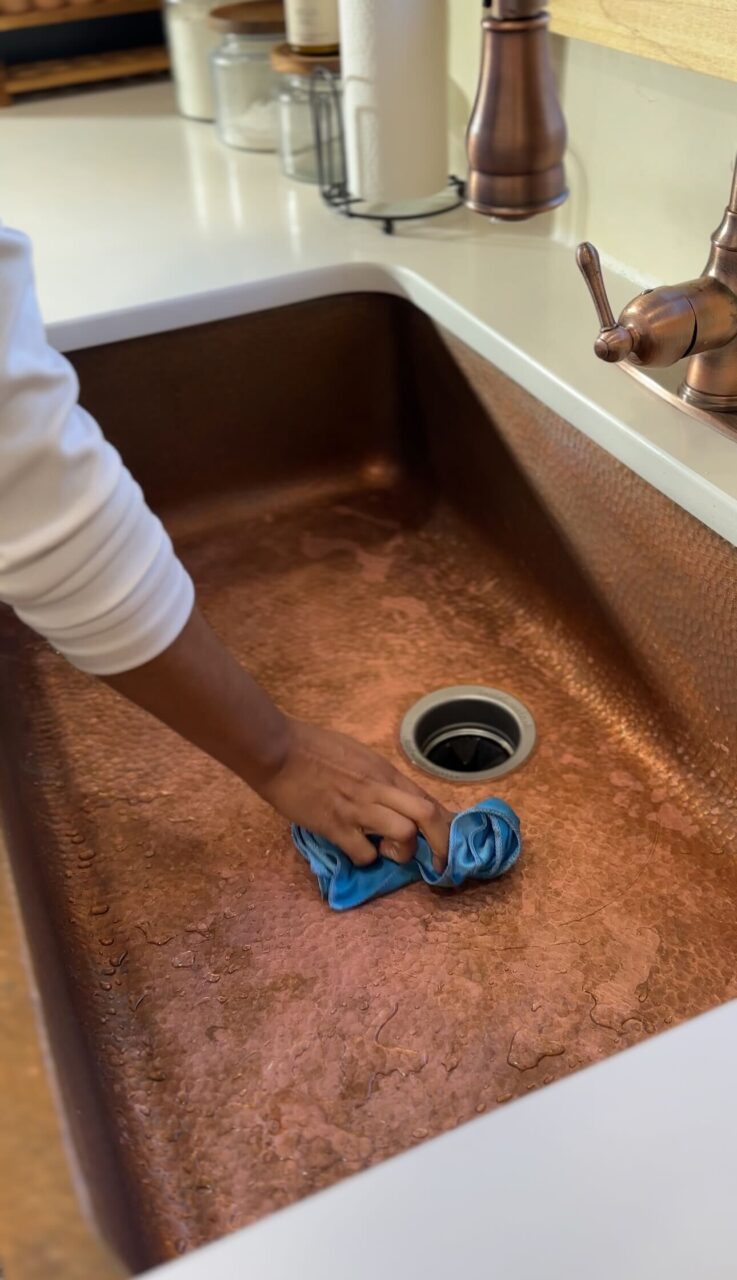 copper kitchen sink with patina being wiped down with rag